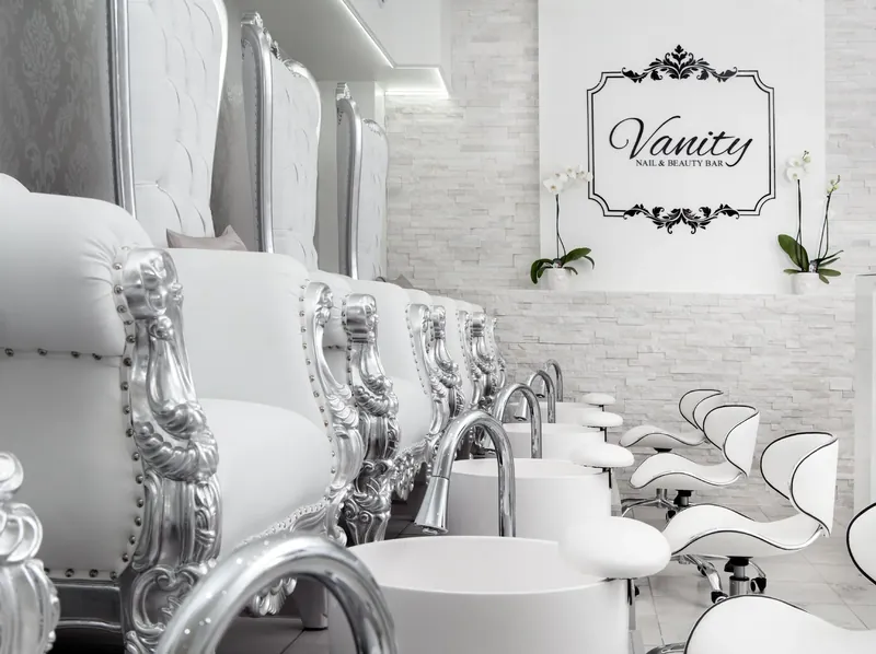 Silver throne pedicure chairs with white basins beside the framed Vanity Nail & Beauty Bar sign and orchids
